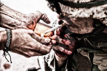 Wounded army soldier, tired military medics with fingers in blood, lighting cigarette with burning match in comrade palms. Psychological pressure, emotional trauma, post-traumatic disorder on war