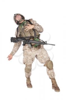 Studio shoot of army soldier in combat uniform and body armor, screaming, clutching chest, dropping weapons and falling down after being fatally shot in military firefight. Marine gets shot in battle