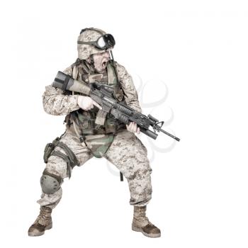 Studio shoot of modern infantry soldier, U.S. marine rifleman in combat uniform, helmet and body armor, screaming and crouching down with assault service rifle in hands isolated on white background