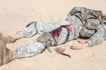 Injured airborne infantry paratrooper shot in leg hip on desert sand. Blood spilled but tourniquet is on, he will be alive