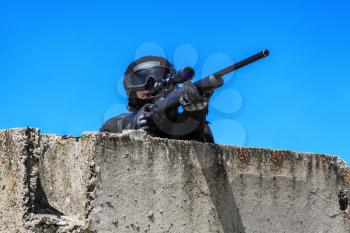 Swat police operator with sniper rifle in black uniforms aiming criminals terrorists waiting in stakeout behind concrete block. Sunny day, low angle