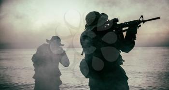 Commando soldiers walking in water, army special operations forces fighters sneaking in darkness, aiming assault rifles and observing shore during amphibious operation on coast at night or dawn