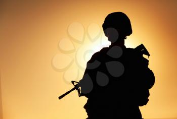 Half-length silhouette of army infantry shooter, special operations forces soldier, Marines rider in combat helmet and ammunition, armed with service rifle standing on background of sunset sky