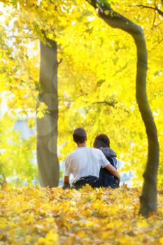 Young happy couple sitting in the autumn park with yellow trees