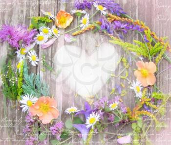 Beautiful wreath of wildflowers from Carpathian Valleys on vintage wooden table. Composition of wild flowers in country chic style on shabby background with heart and place for your text or picture.