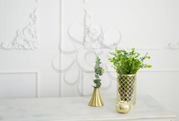 Brass golden candlestick. Green decorative plants in brass vase.
