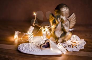 Golden figure of an angel with lights of the garland against a background of ceramic handmade hearts. Valentine's day concept.