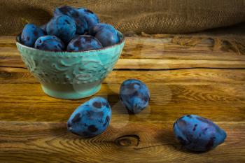Fruit plums prunes in turquoise cup on old dark wooden background. Selective focus