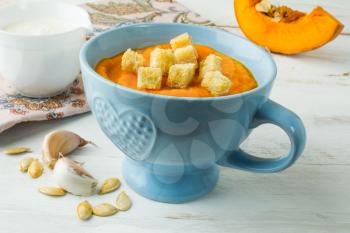 Creamy pumpkin squash vegetable soup with garlic croutons in a blue bowl and pumpkin slice on white wooden background