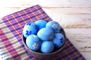 Blue Easter eggs in a purple bowl on a checkered napkin on a white wooden background. Easter 