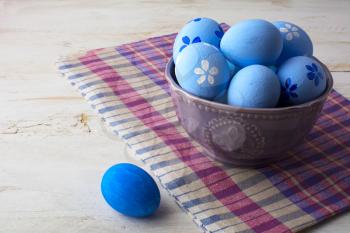 Light blue Easter eggs in a purple bowl on a checkered napkin on a white wooden background. Easter background. Easter eggs. Easter. Easter hunt. Easter symbol.  Easter card. Easter greetings. Happy Easter