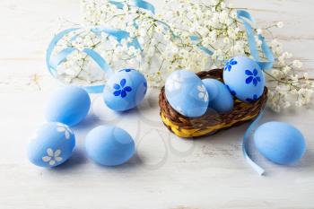Blue Easter eggs in a small wicker basket and small white baby's breath flowers on white wooden background