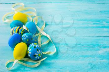 Row of blue hand-painted Easter eggs with satin ribbon on blue wood plank. Easter background. Easter symbol. Top view with copy space