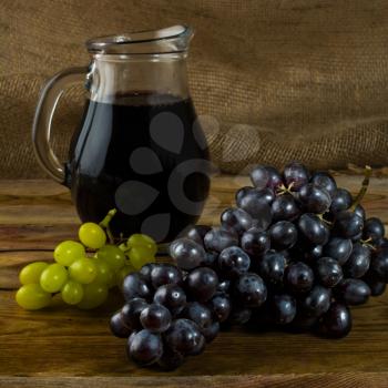 Bunch of grapes and a Wine jug  on a dark wooden background. Bunch of grapes. Cluster grapes.  Bunch grapes. Grapes. Grape. Glass of wine. Glass wine. Grape vine
