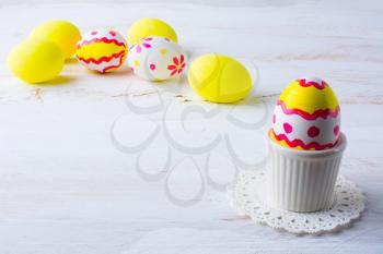Decorated Easter egg in an egg cup on a white wooden background, white pink red yellow eggs in the background, space for text, copy space