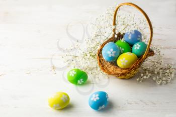 Decorated Easter eggs in the basket with small white baby's breath flowers on a white wooden background, space for text, copy space