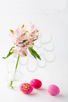 Easter hand-painted pink eggs with light delicate pink flowers in a glass vase on white background. Easter background. Easter symbol. Top view with copy space. Vertical