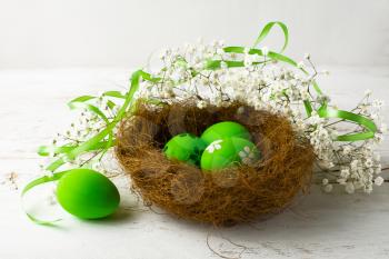 Green Easter eggs in a nest with green satin ribbon on a white wooden background