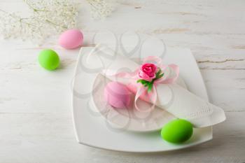 Pink and green Easter table place setting with plate, napkin, pink and green Decorated Easter eggs on white wooden background