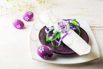 Purple mauve lilac Easter table place setting with plate, napkin and purple Decorated Easter eggs on white wooden background