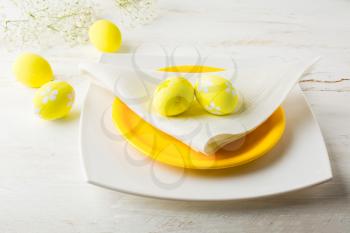 Yellow Easter table place setting with plate, napkin and Yellow Decorated Easter eggs on white wooden background
