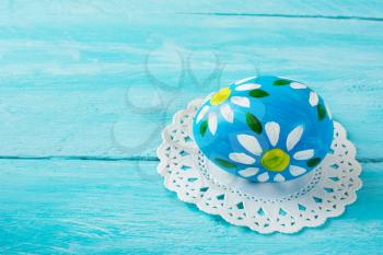 Нand-painted blue Easter egg with floral design on a blue wood plank background. Easter background. Easter symbol. Copy space