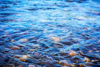 Defocused blue water surface background. Stony bottom of a clear mountain river. Flecks of sunlight and ripples on the water of river. Water background.  Water surface texture.