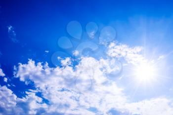 Idyllic clear blue sky with fluffy clouds and sunbeams. Beautiful cloudy blue sky background