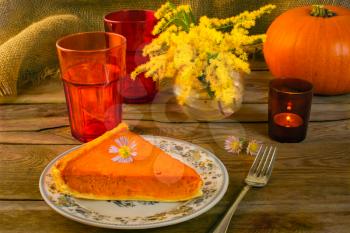 Pumpkin pie slice, fork, plate, vase, yellow flowers, mimosa purple daisies, red glasses, candleholder, sackcloth, wood background