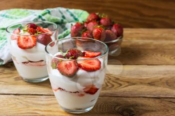 Summer dessert with whipped cream and strawberry on wooden background . Layered dessert with fresh ripe strawberry.