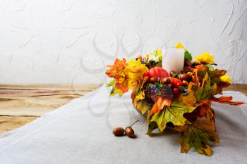 Thanksgiving centerpiece with white candle and silk fall leaves . Thanksgiving background with fall decor. Fall background. Copy space.