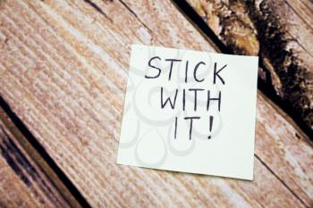 Handwritten motivational message on the white paper. Stick with it message on the paper with retro wooden bark background. Conceptual message written on the white paper.