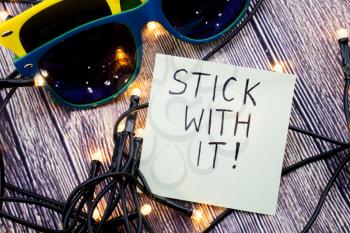 Stick with it motivational concept in business on notepaper. Two sunglasses of different colors with retro wooden background. LED lights are shown in various order. Business concept.