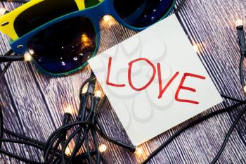 Love handwritten on white paper with red color. Two sunglasses in various combinations of colors with lights set in random order with wooden background. Valentine Day or love concept.