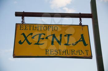Paleokastritsa, Cofru, Greece- MAY 10, 2018Restaurant wooden hanging sing post. Yellow board with black letters chained to brown stick announcing a place where you can buy some food