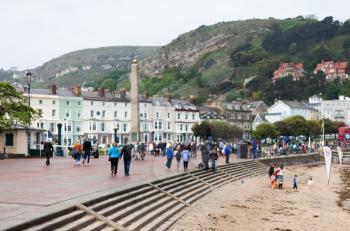 LLandudno, Wales, UK - MAY 27, 2018 City buildings with crowd of people and mountains in the background. People are walking on sidewalk. Holiday concept with mountain houses. Old looking buildings in town. Houses on the hill.