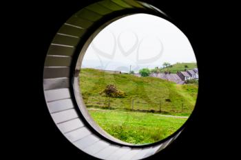 Green grass on the meadow field with sea in the background. Composition through the round window. Scenery with meadow and beautiful nature. Beautiful landscape composition with blue sky.