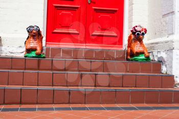 House entrance with red door and two dragon statues on the floor. Decorative dragons with sunglasses and hats greeting visitors. Home outdoor decor stone figure