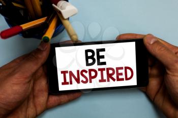 Conceptual hand writing showing Be Inspired. Business photo showcasing extraordinary quality as arising from some creative impulse Man holding cell phone looking messages apps cup markers