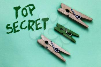 Text sign showing Top Secret. Conceptual photo telling someone important data or information that he cant tell Three brown green vintage clothespins clear background Holding things