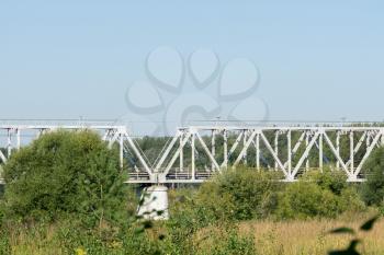 View to a metal railroad bridge across small river over blue sky.