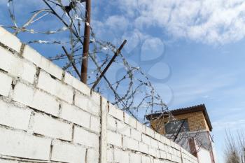 Old barbed wires and white brick wall against blue sky.