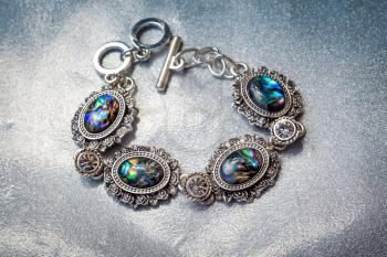 Fashion retro silver bracelet decorated with dark rainbow abalone shell on glitter background.