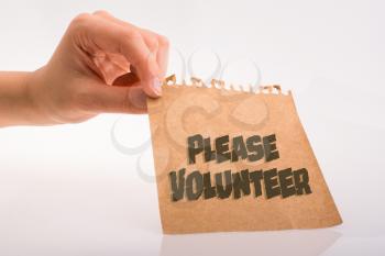 Hand holding paper with PLEASE VOLUNTEER wording on white