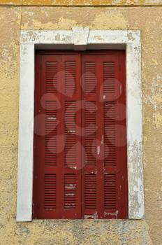 Red window shutter and weathered chipped paint wall.