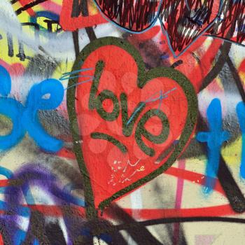 Heart graffiti over messy tagged urban wall background.