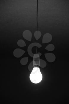 Incandescent bare light bulb glowing in dark room. Abstract background.