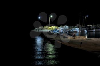 Empty pier and boats dark night. Street light reflections on black sea.