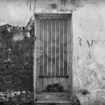 Rusty door and textured broken wall abandoned house exterior. Black and white.