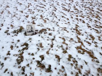 Solitary headstone at graveyard cemetery with snow on white winter day